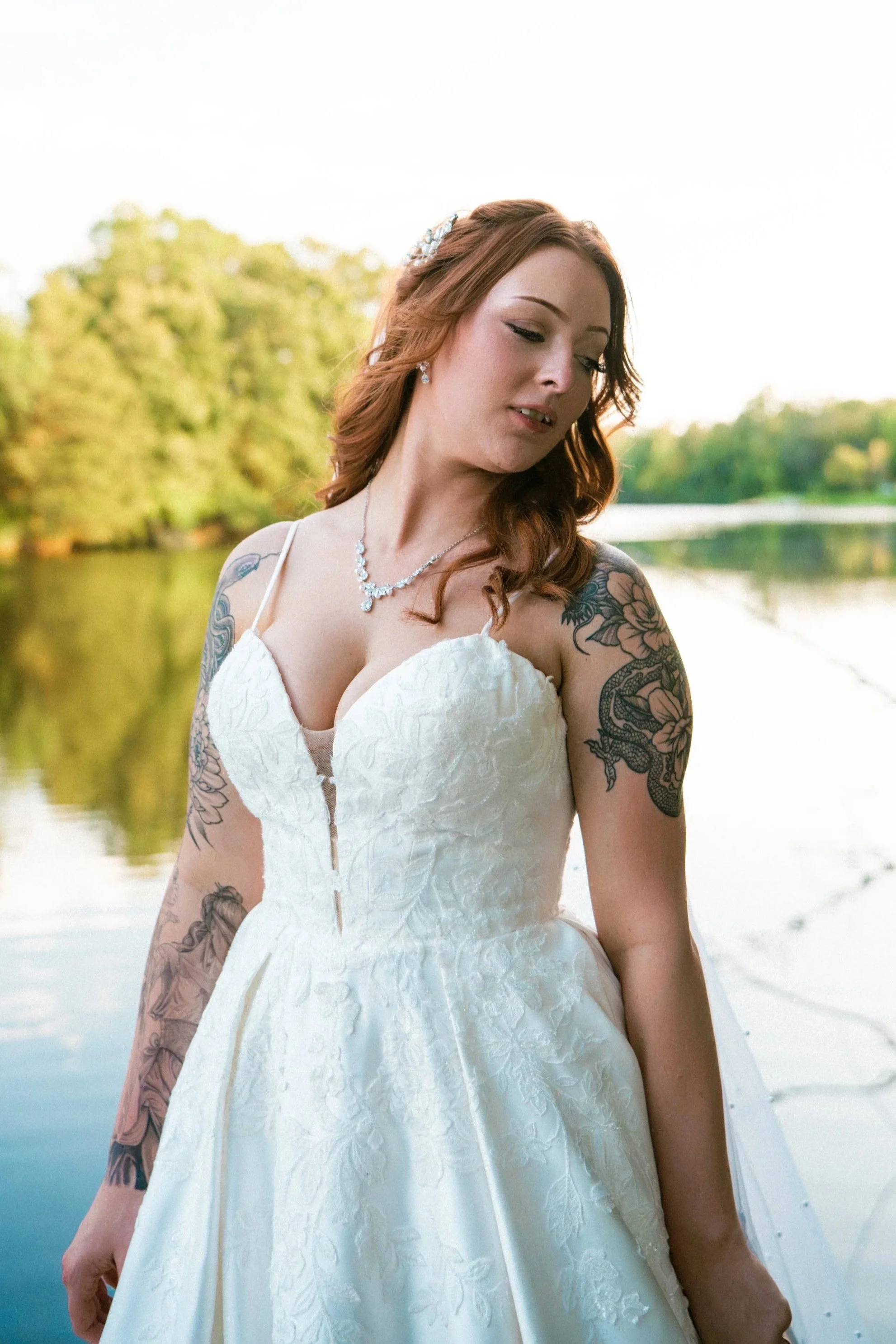 A bride in a lace wedding dress standing beside a lake